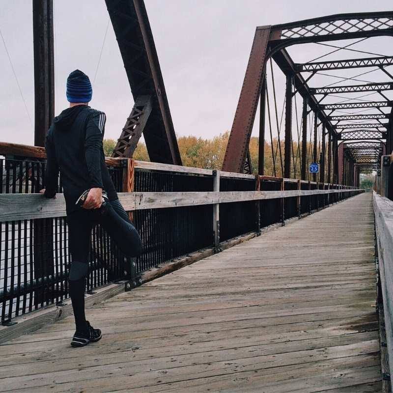 male runner stretching on a bridge
