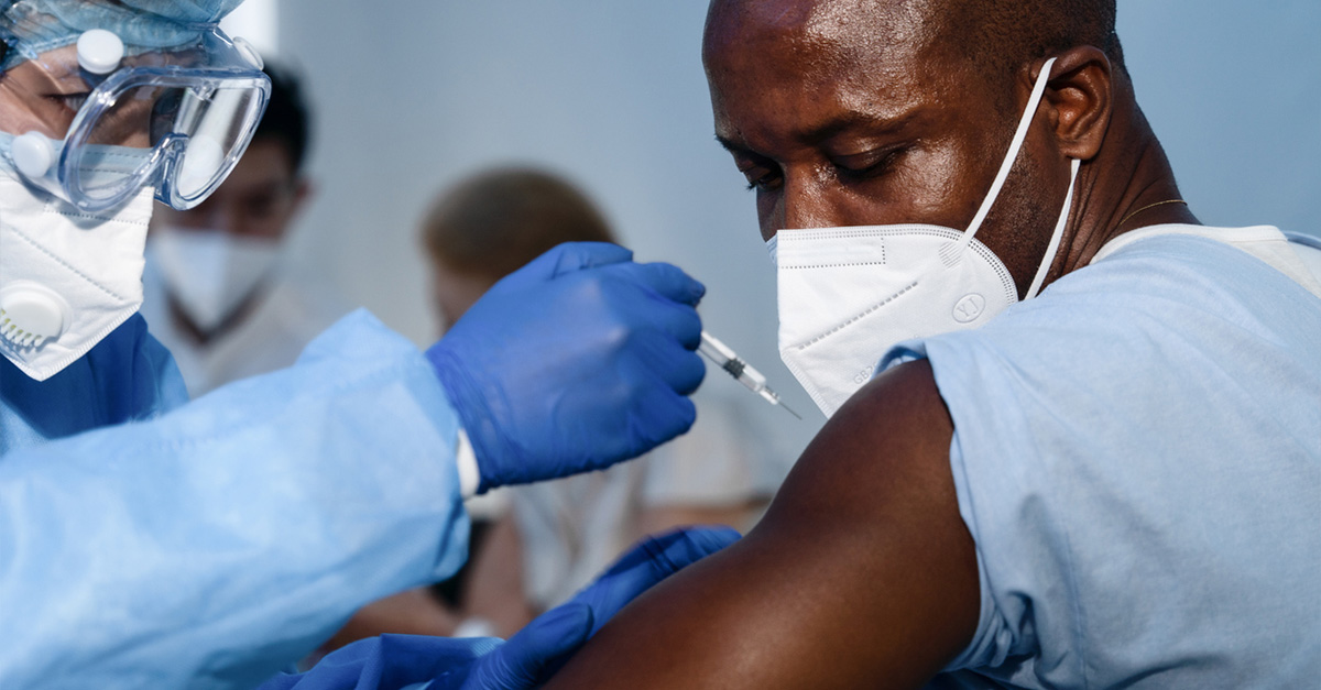 African Americam man looking at coronavirus covid-19 syring while medical staff injects vaccine to arm muscle to build immunization of coronavirus covid-19 for him.